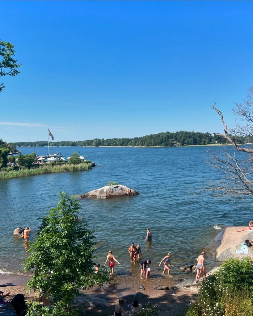 Small sandy beach with calm water and green trees in Vaxholm, Sweden